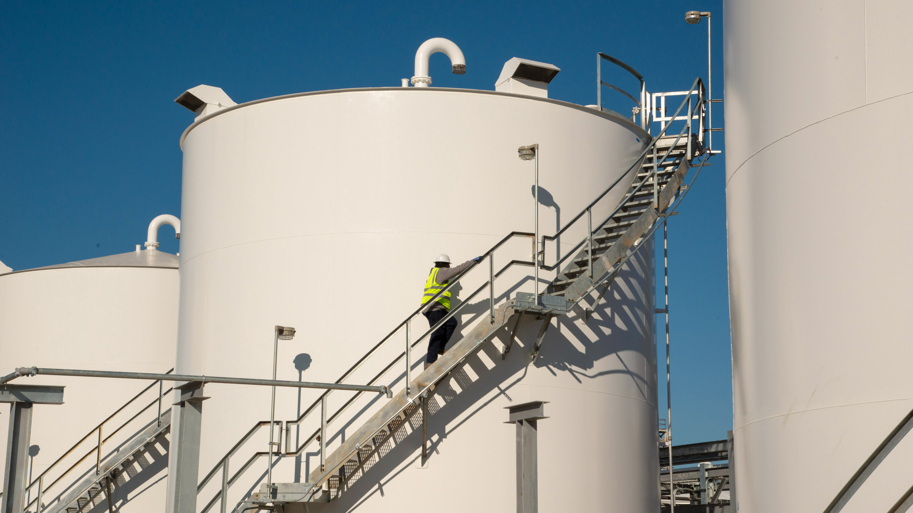 a worker in safety gear climbing the stairs to the top of an fuel tank